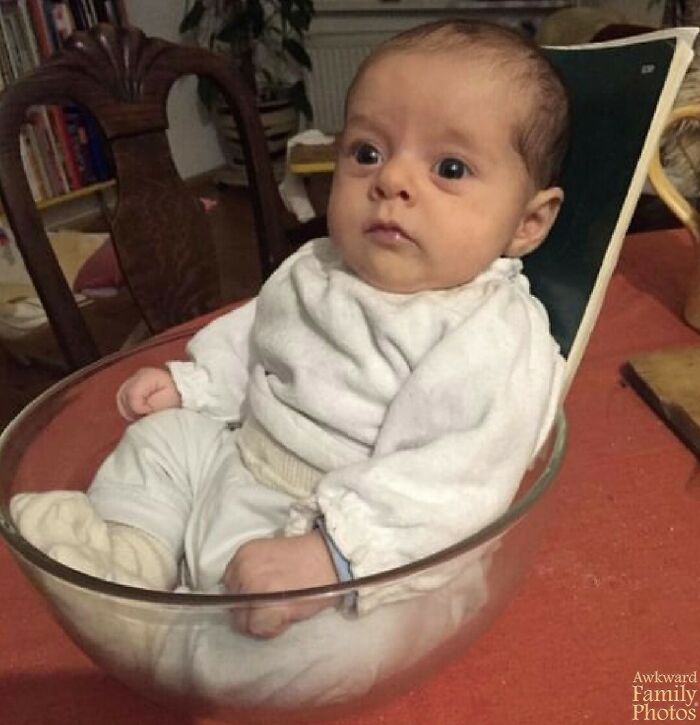 Baby sitting in a glass bowl on a table, capturing an awkward family photo moment.