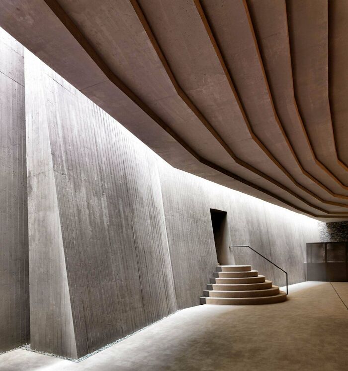Minimalist concrete interior with angular walls and curved ceiling, evoking evil auras of supervillain headquarters design.
