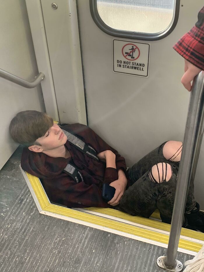 Passenger sitting on train stairs despite warning sign, showcasing public transport behavior.