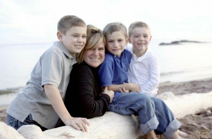 Family posing awkwardly on a beach log, with three boys and a woman smiling for a photo.