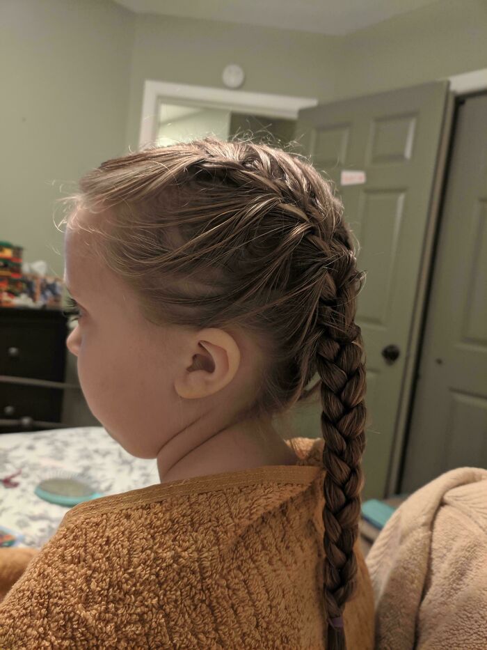 Niña con trenza hecha por su papá en un momento tierno y divertido de crianza, mostrando amor paternal y cuidado.