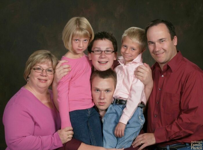 Awkward family photo with six people, some smiling, wearing casual attire against a plain backdrop.