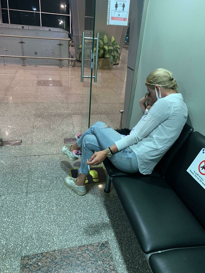 A woman in an airport waiting area, sitting with her feet up on a seat, looking tired and frustrated, depicting annoying plane passengers.
