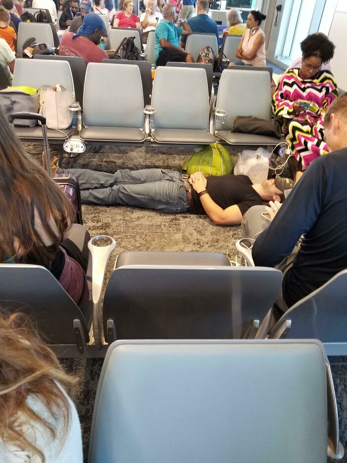Passenger sleeping on the airport floor next to seats, illustrating annoying plane passengers in crowded waiting area.