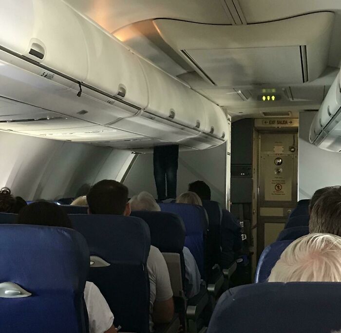 Passenger standing in aircraft aisle facing overhead bin, illustrating annoying plane passengers behavior.