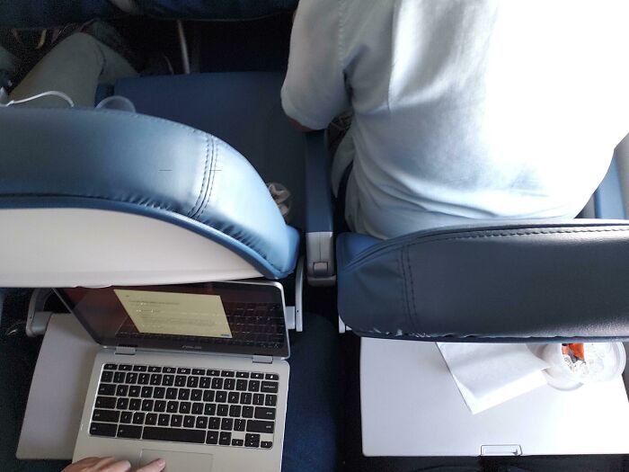 Annoying plane passengers with seat reclined, disrupting laptop work on a flight, illustrating in-flight discomfort.