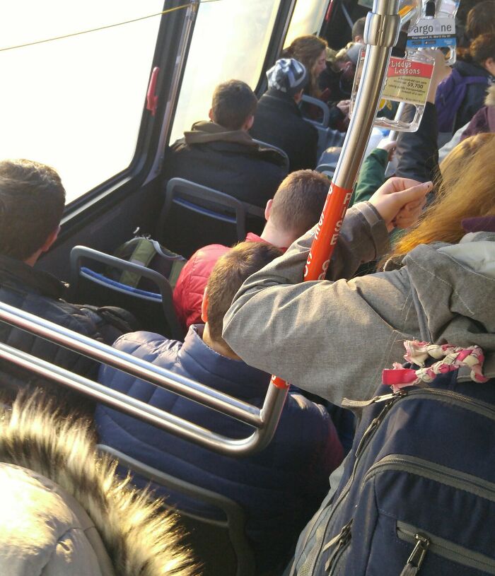 Crowded bus interior with standing passengers holding onto a pole, illustrating public transport challenges.