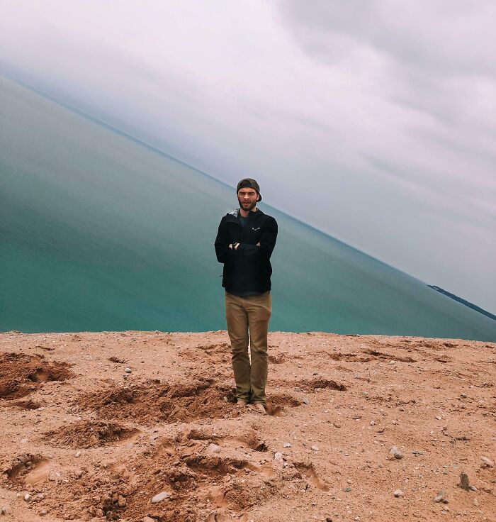 Man standing on a tilted beach cliff with ocean background, interesting not photoshopped perspective.