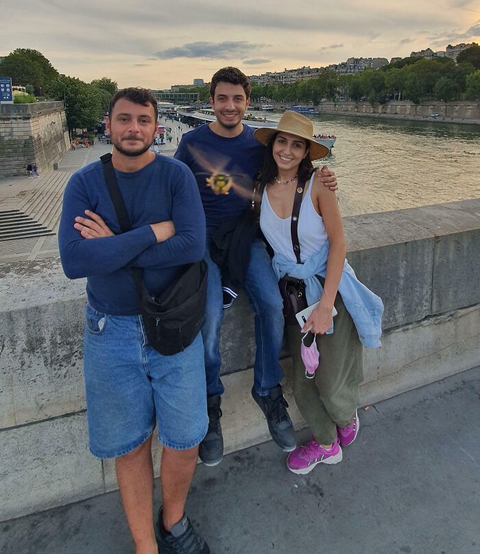 Three friends posing on a riverside wall at sunset, showcasing interesting candid moments in a not photoshopped photo.
