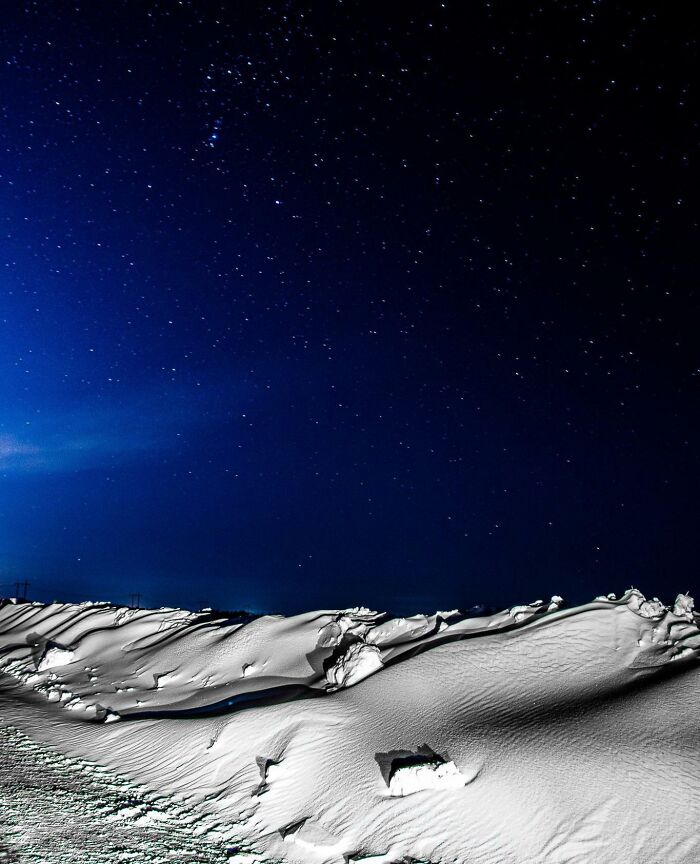 Snowy landscape under a starry night sky, showcasing an interesting, not photoshopped photo effect.