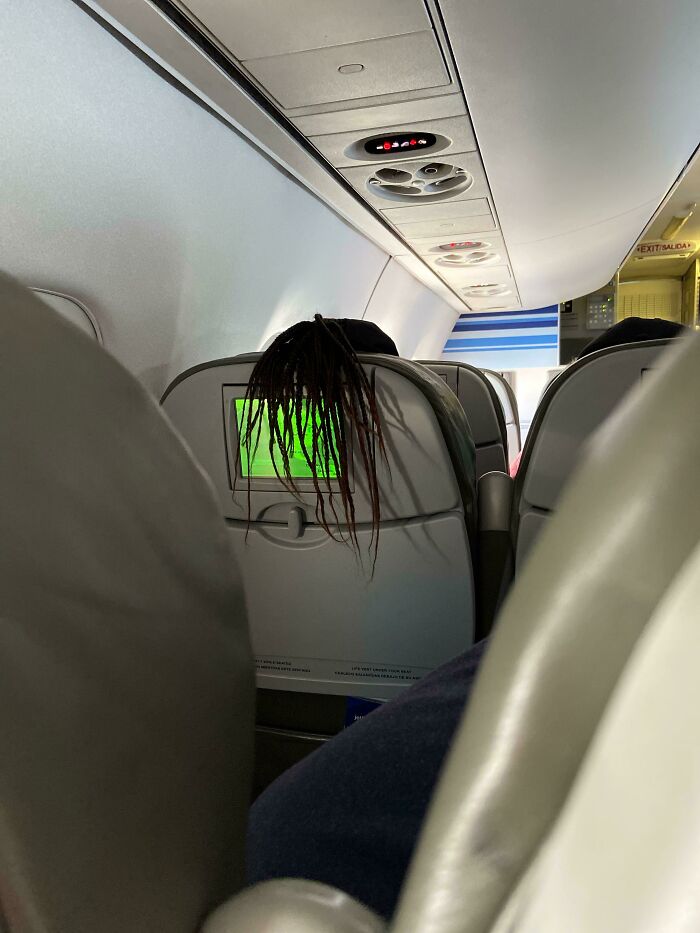 Hair drapes over an airplane seat, obscuring the screen, epitomizing annoying plane passengers.