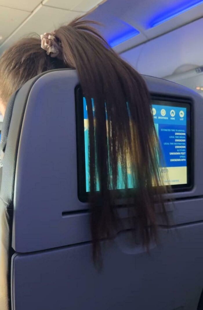 Hair draped over airplane seat blocking screen, illustrating annoying plane passengers.