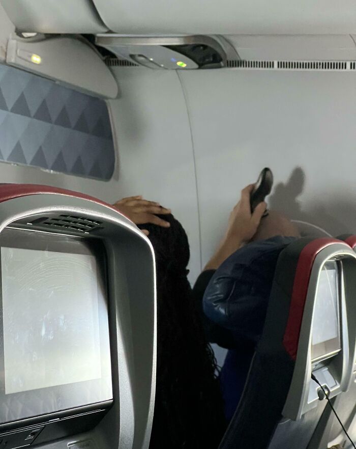 Passenger using phone flashlight on a plane, possibly causing discomfort to others; an example of annoying plane passengers.