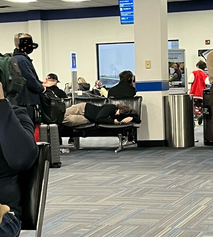 Passenger sleeping across airport seats, creating limited seating for others.