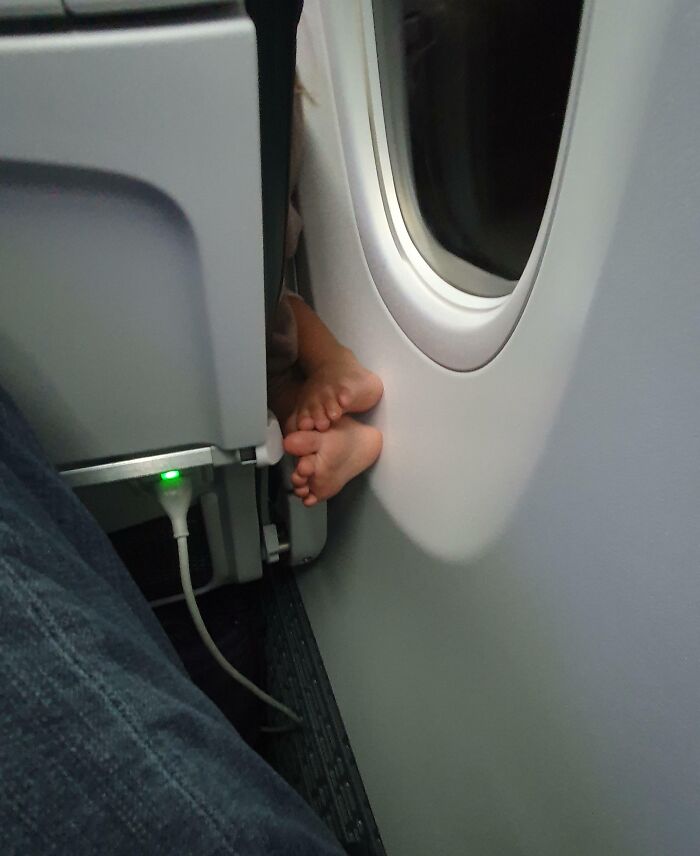 Child's feet on airplane window, highlighting annoying plane passengers.