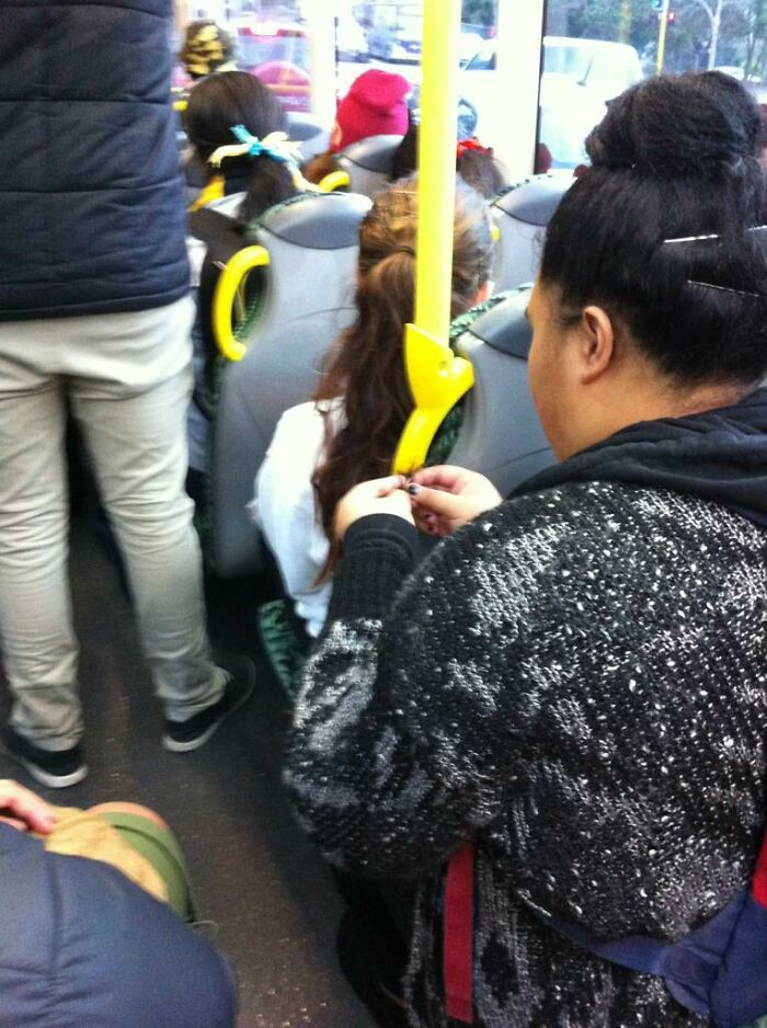 A woman braiding another's hair on public transport, passengers around seemingly unaware.