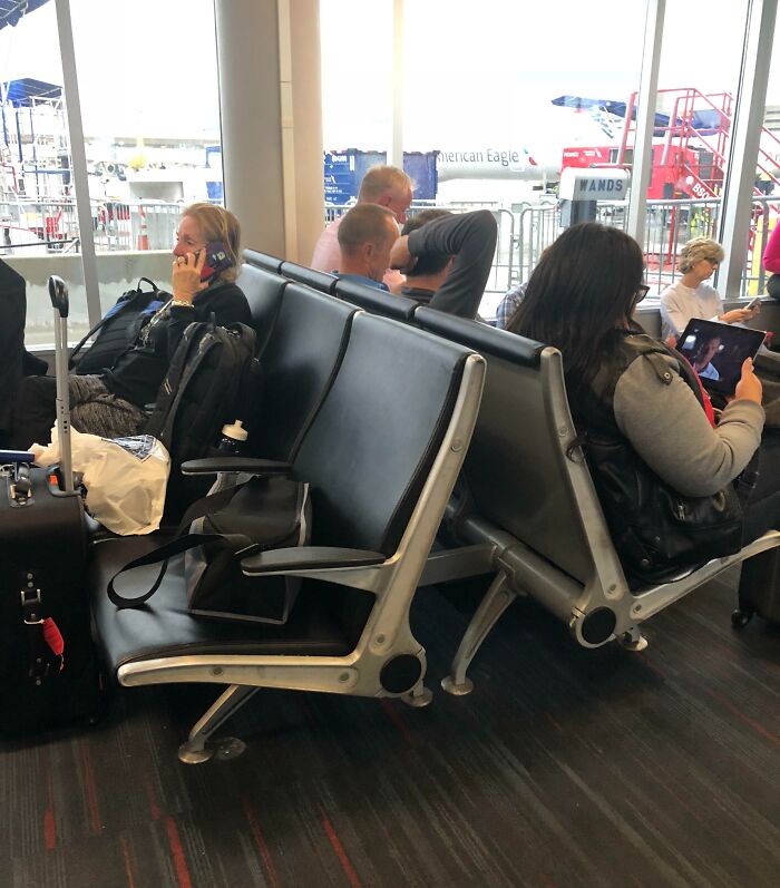 Passengers on airport benches with luggage, phones, and tablets, depicting annoying-plane-passengers scenario.