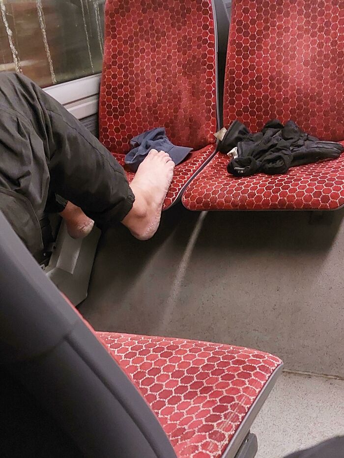 Barefoot passenger on public transport with items on adjacent seat.