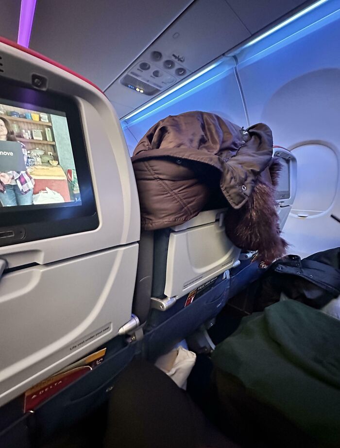 Airplane seat with coat draped over seatback, highlighting annoying plane passenger behavior.