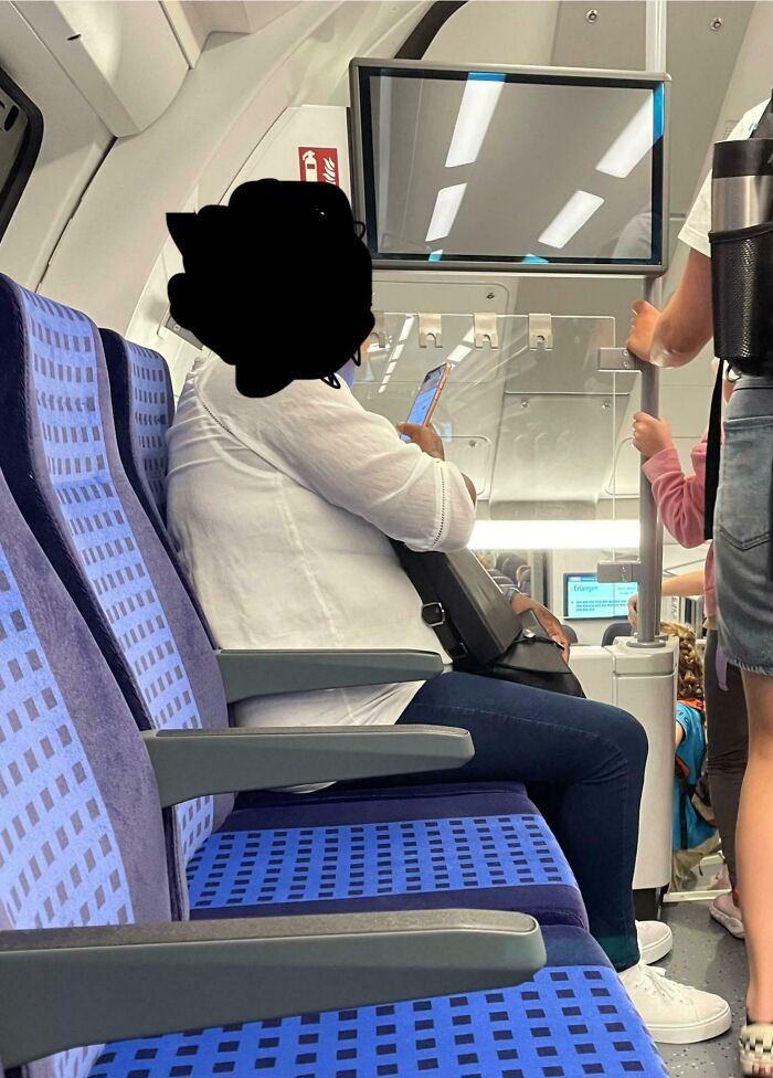 Public transport passenger taking up extra seats, using a phone on a train.