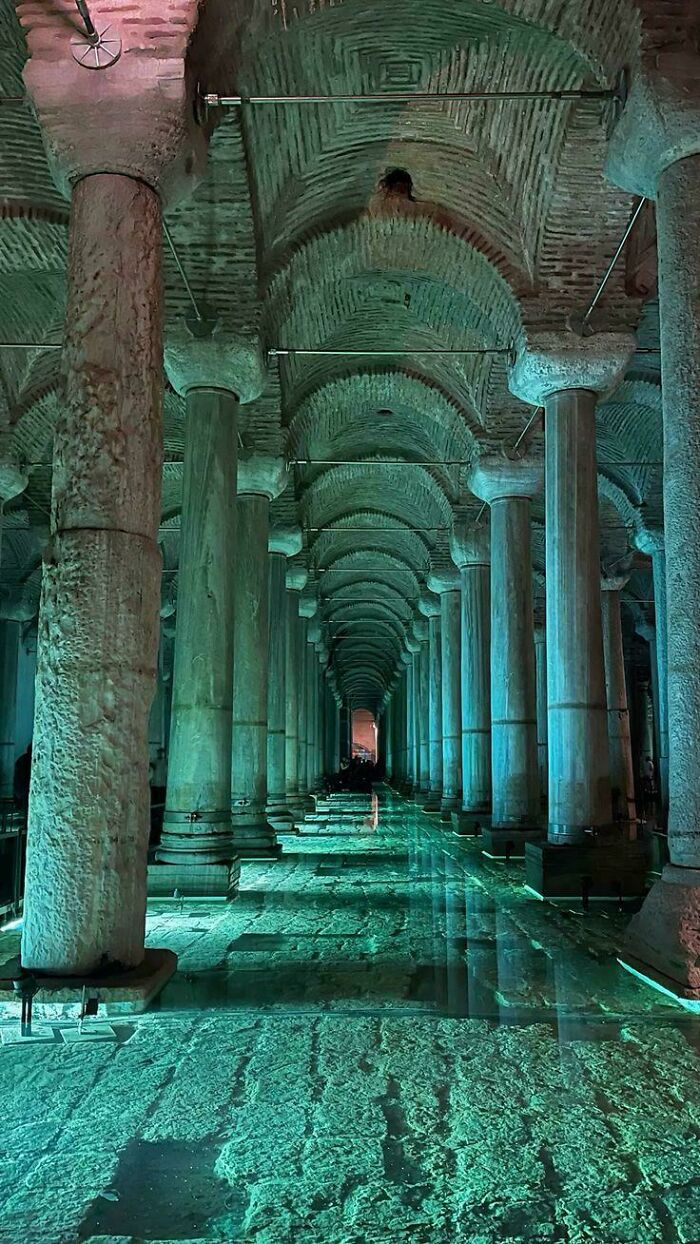 Ancient architectural feat showing a columned hallway with green lighting and reflective water on the stone floor.