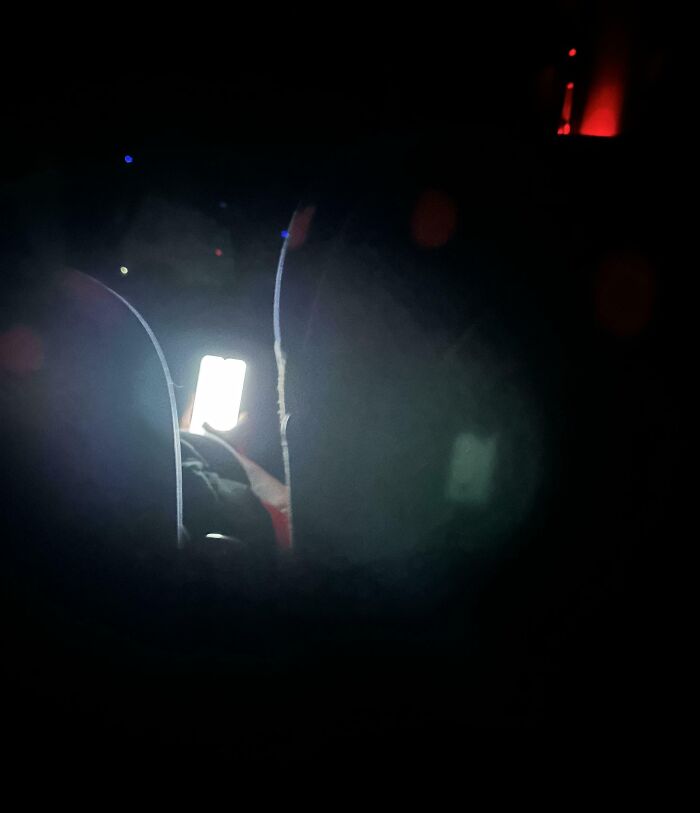Passenger using a bright phone screen in a dimly lit public transport setting, causing annoyance to others.