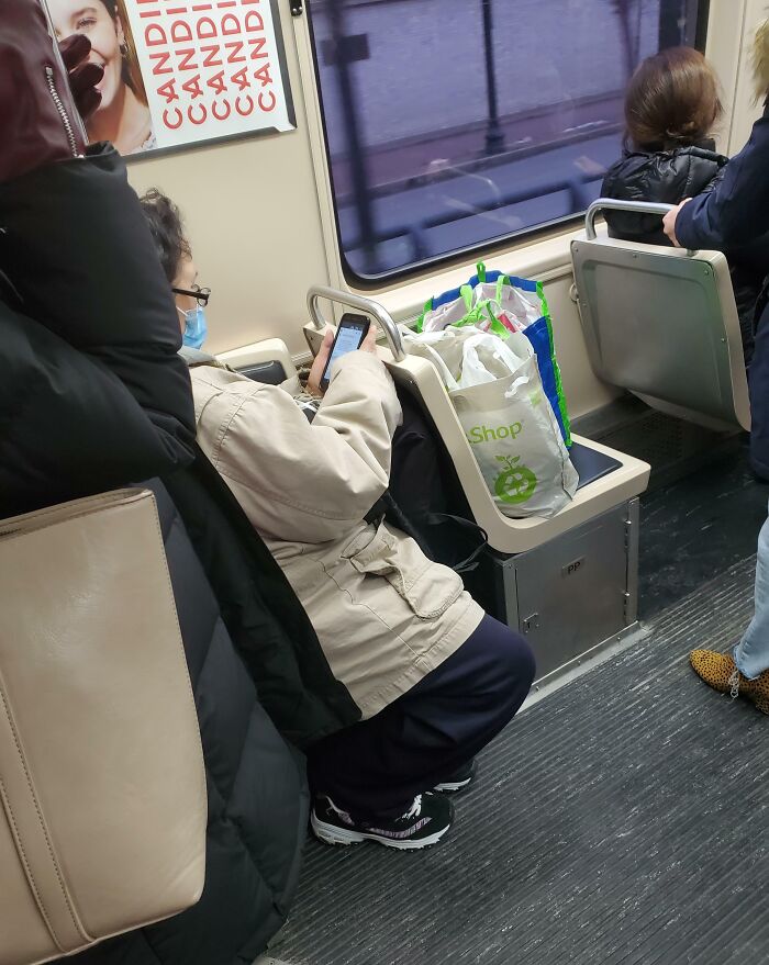 Public transport passenger occupies seat with bags, using phone.