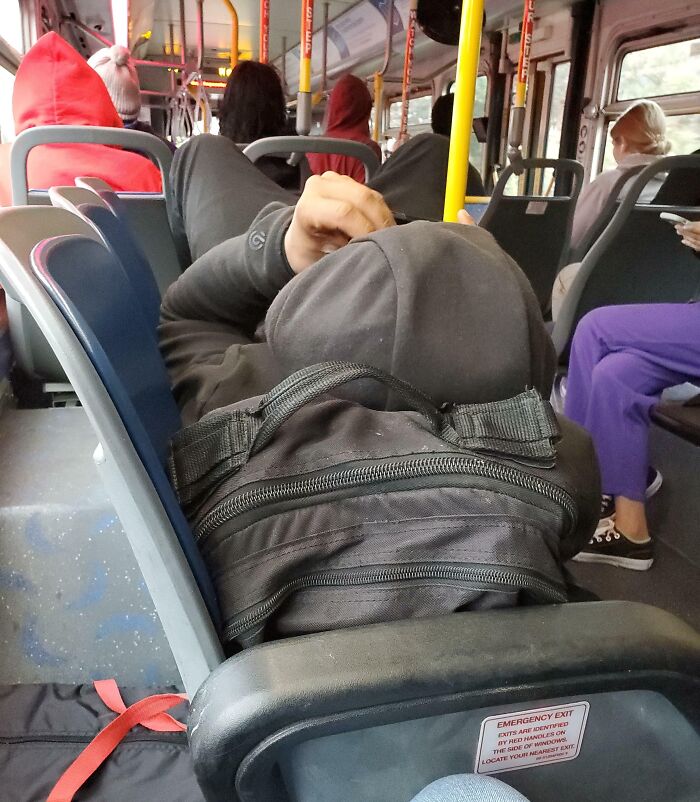 Person lying down across bus seats, blocking others, illustrating public transport passenger behavior.
