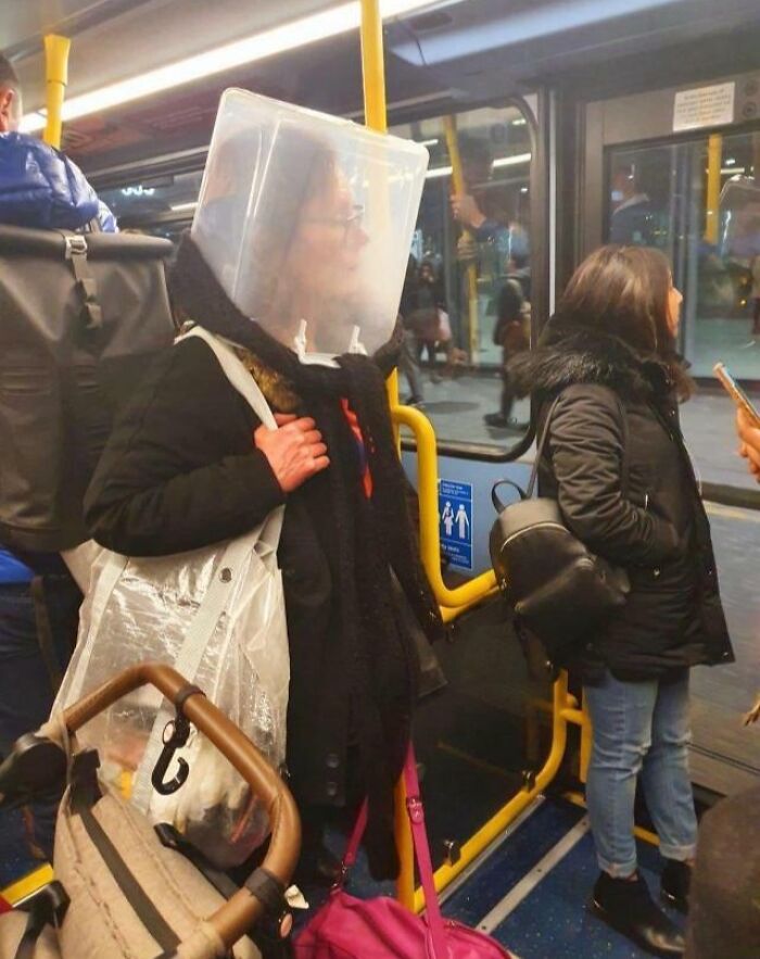 Public transport passenger with a plastic container on head, standing near another passenger with a phone.