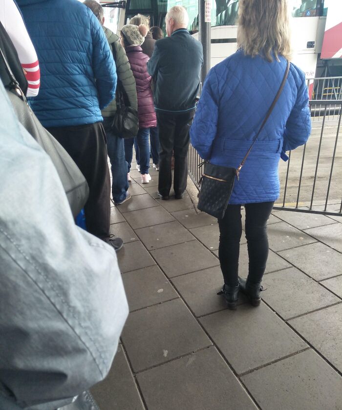 Passengers in line at a bus stop, highlighting public transport challenges.