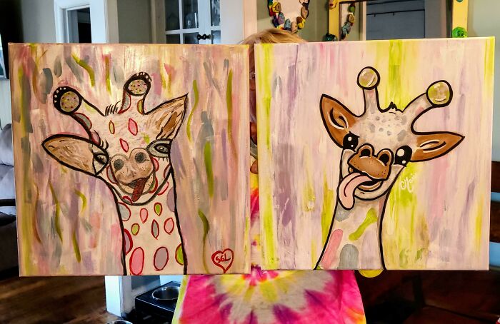 Colorful giraffe paintings held by a person in a tie-dye shirt, showcasing creative artwork by amazing mothers-in-law.