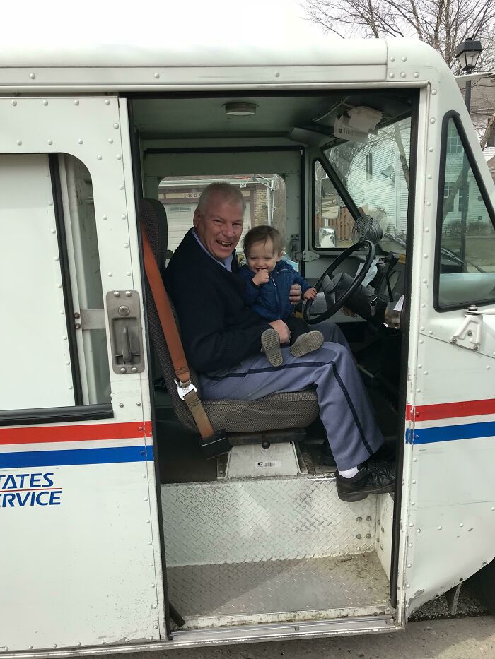 A smiling man sitting in a mail truck with a child, showcasing an amazing bond.