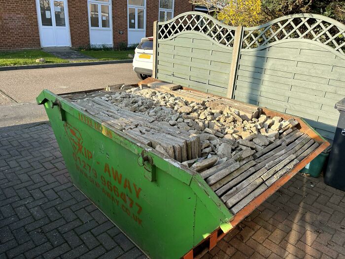Green skip full of rubble and wooden planks on a driveway, showcasing a hilarious in-laws DIY mishap.