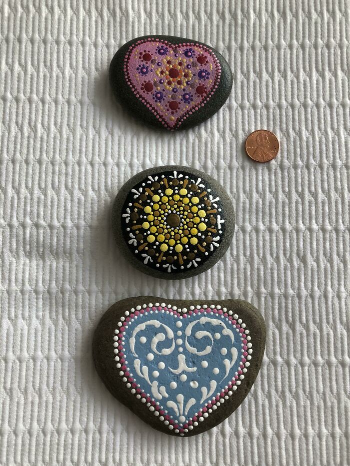 Decorative heart-shaped stones painted with intricate designs alongside a penny, highlighting amazing creativity.