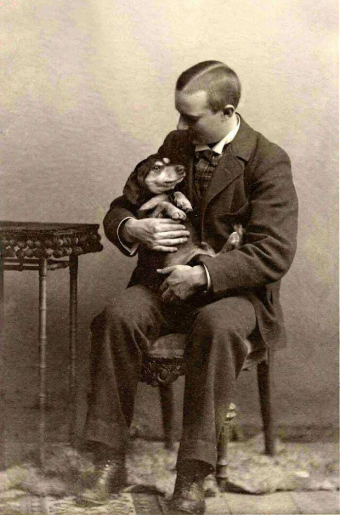 Vintage photo of a man in a suit affectionately holding his dog, showcasing pets as family.