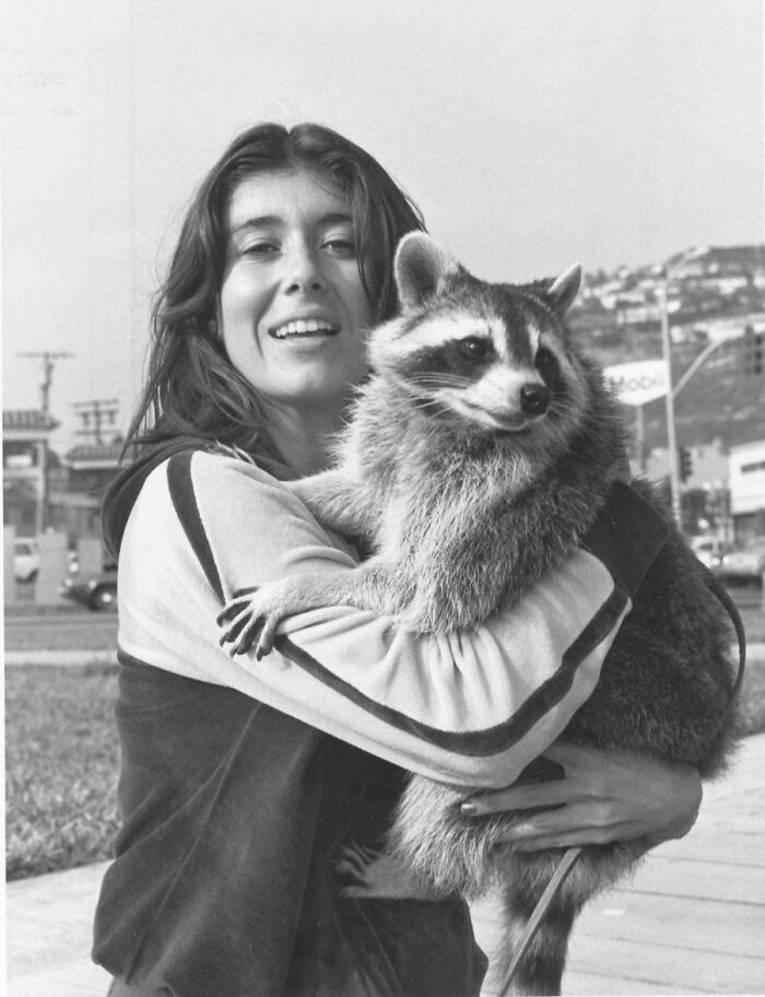 Woman smiling and holding a raccoon, demonstrating the timeless bond between pets and family.