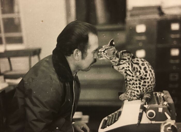 Man nose-to-nose with a spotted cat on a typewriter, vintage photo showing pets as family.