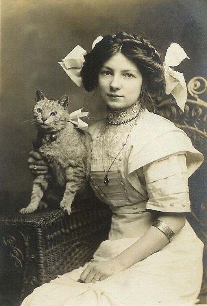 Woman in vintage dress holding a cat, showing pets as family in historical sepia photo.