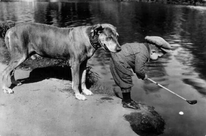 Vintage photo of a young boy fishing by a lake with his dog, highlighting pets as family.