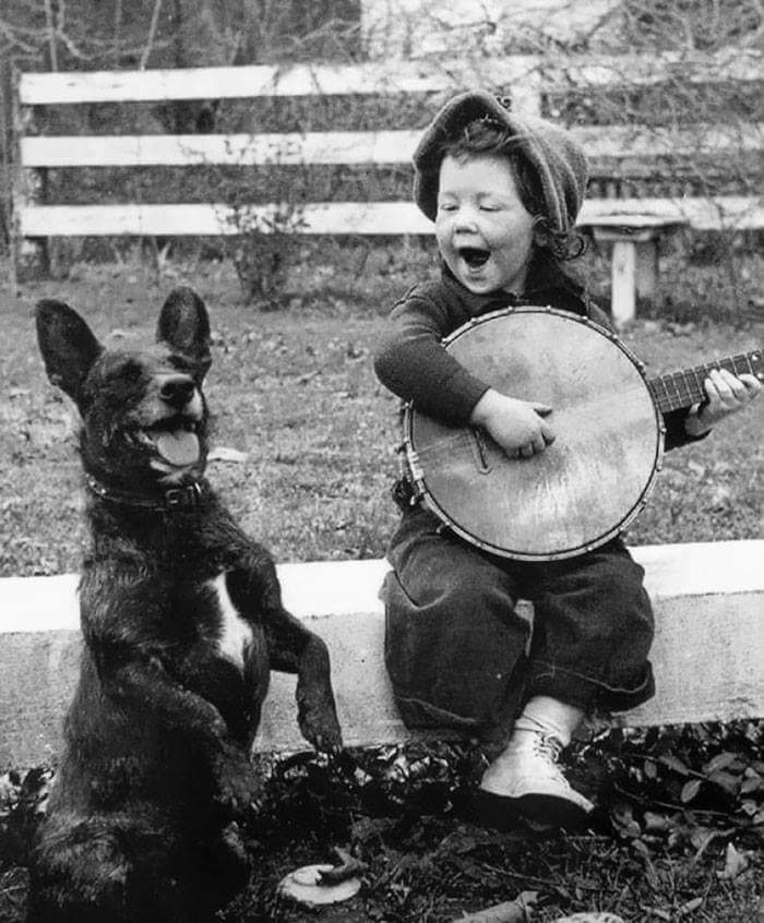 Child plays banjo next to a happy dog, showcasing vintage bond with pets as family.
