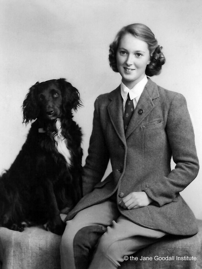 Vintage photo of a woman in a suit sitting with a black dog, highlighting the timeless bond between pets and family.