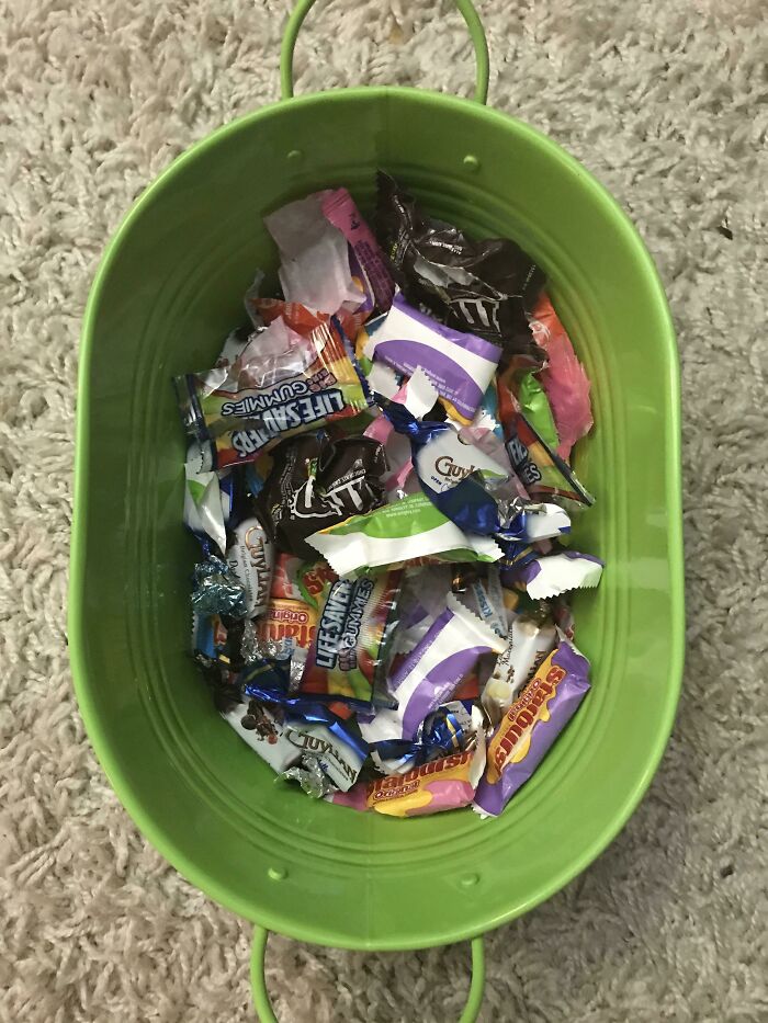 Green container filled with assorted candy wrappers, representing infuriating family members' leftover mess.