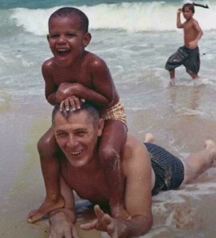 A child laughing on a man's shoulders at the beach, enjoying the waves, illustrating unseen historical moments.