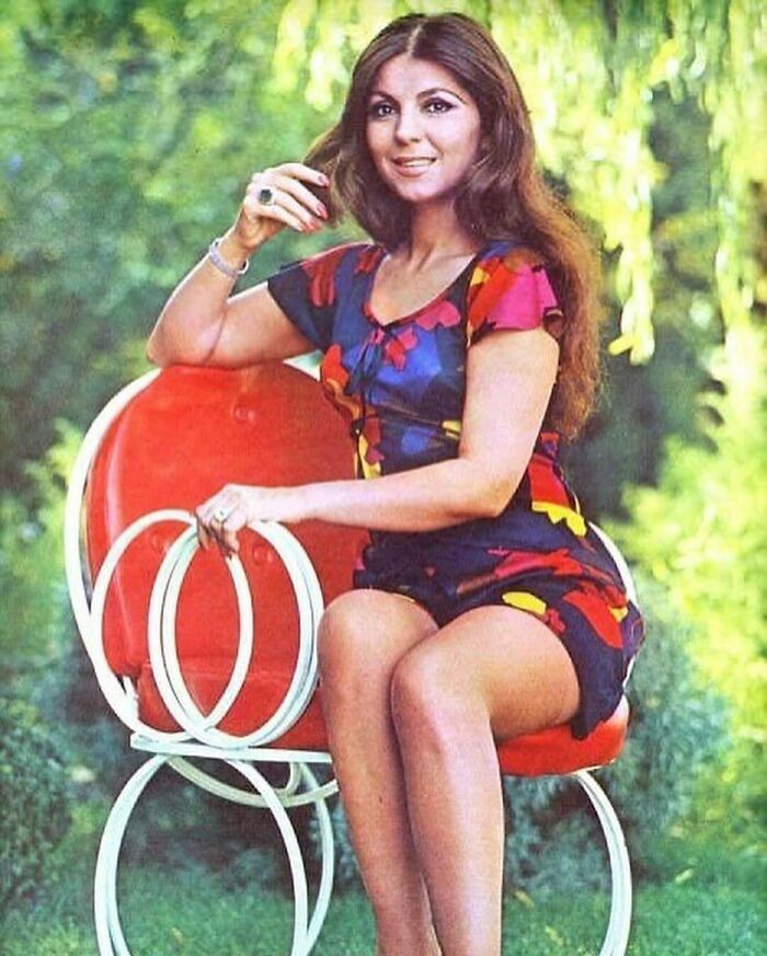 Woman in a colorful dress sitting on a red chair in a garden, showcasing a scene not typically seen in history textbooks.