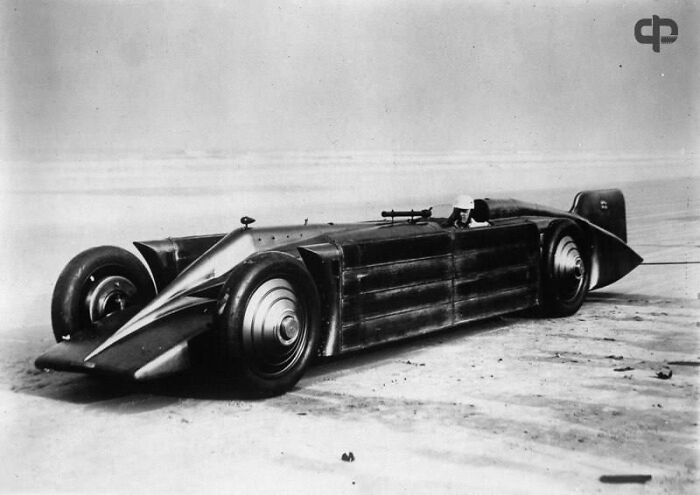 Vintage streamlined race car on a sandy track, showcasing early motorsport engineering not seen in history textbooks.