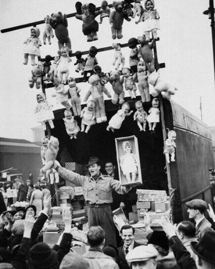 Vintage market scene with a salesman surrounded by dolls and toys, engaging with a crowd.