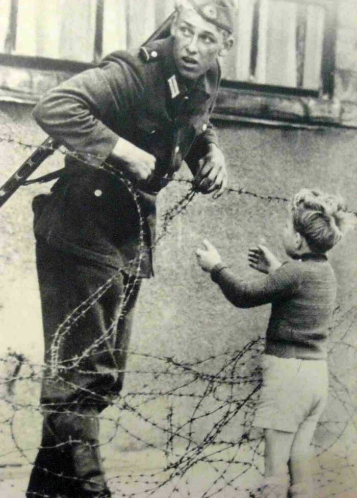 Soldier helping a child across barbed wire, a historical moment not commonly seen in textbooks.