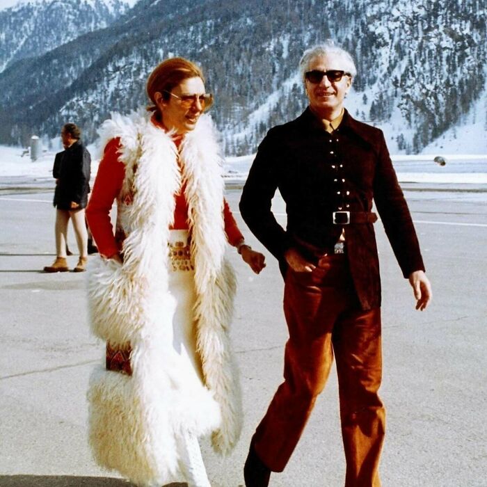 Vintage couple in stylish winter attire walking, snow-covered mountains in background; rare historic photo.
