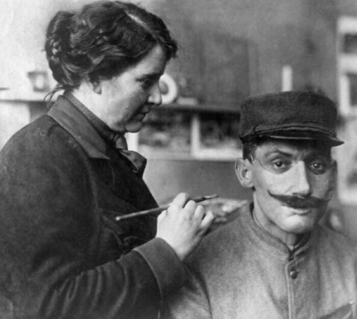 Historical photo of a woman painting a prosthetic face on a WWI soldier.