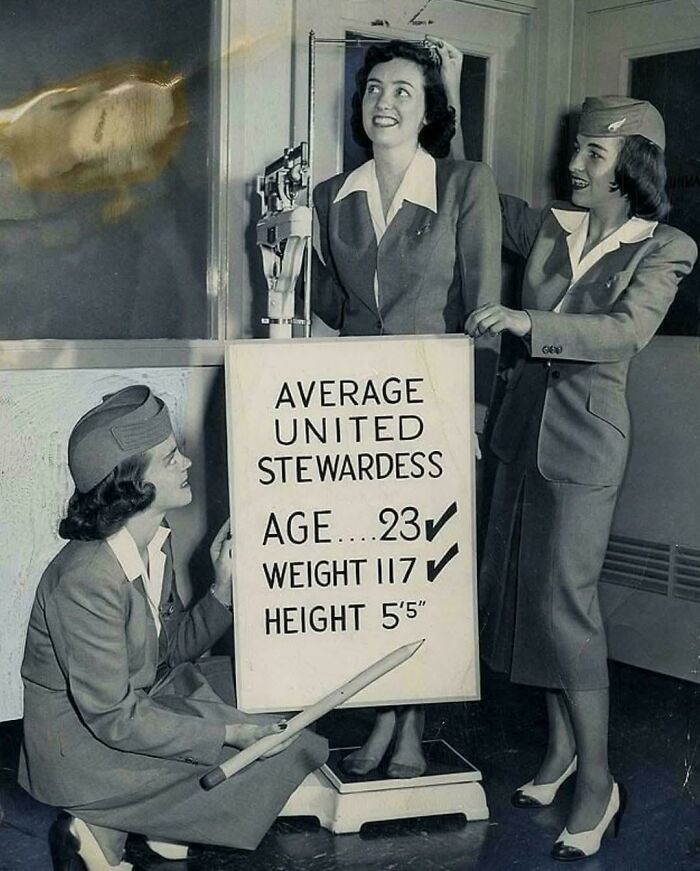 Vintage photo of stewardesses with a board listing average age, weight, and height.